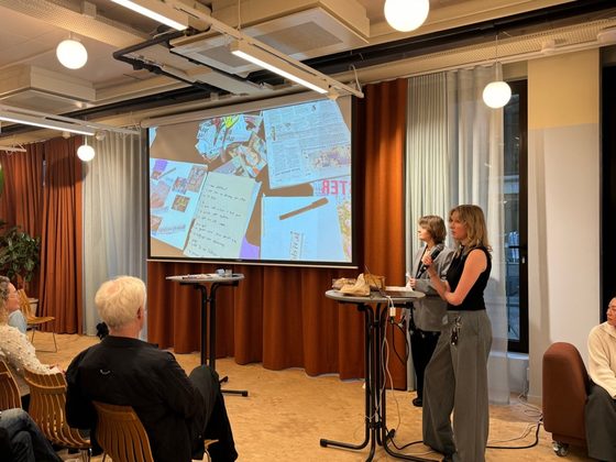 Ingrid presenterer med mikrofon foran et lerret som viser en collage av papirmateriale.