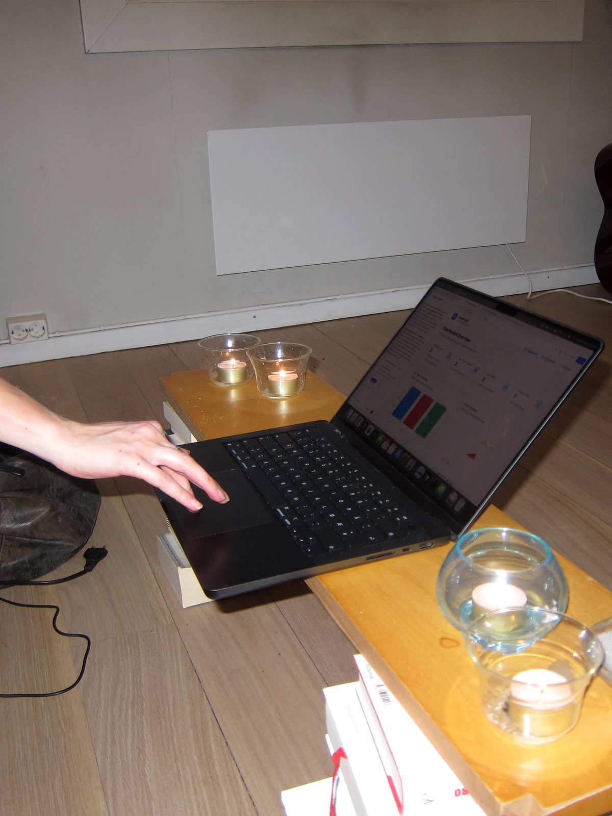 En hånd på en bærbar PC som står på gulvet mellom telys, sent på kvelden.